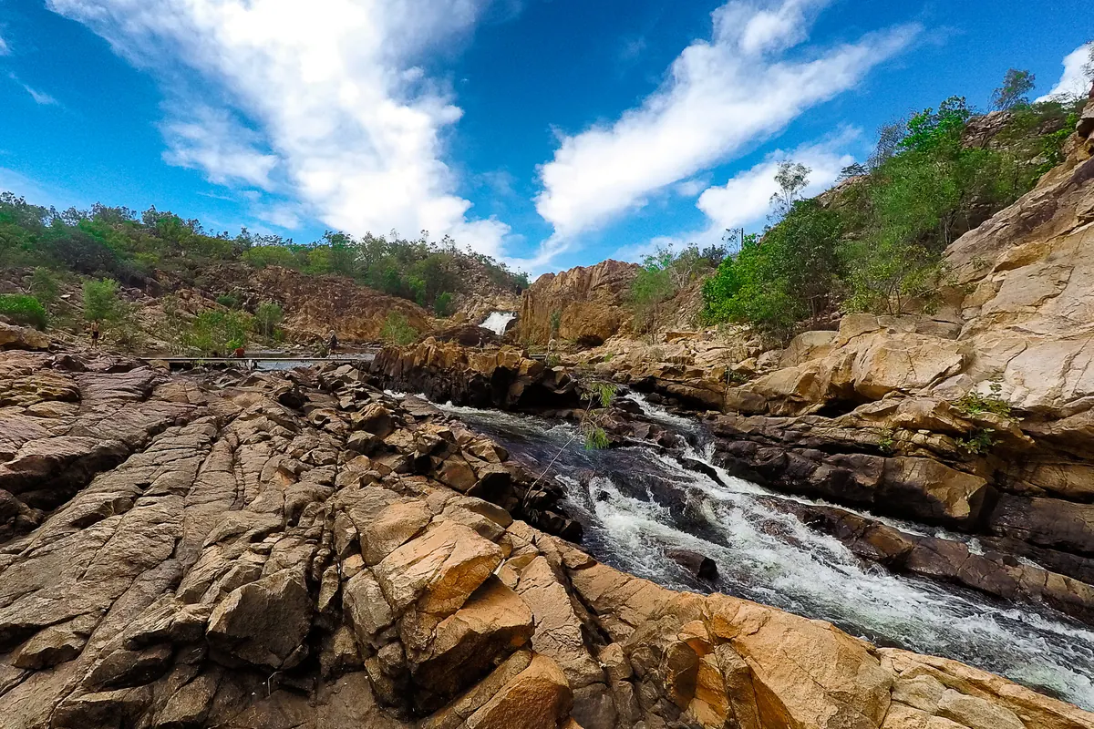 Water spills over layered orange rock ledges at Edith Falls, also called Leliyn, under a blue sky with streaky cloud (a swimming spot in the Katherine region, not the arena)